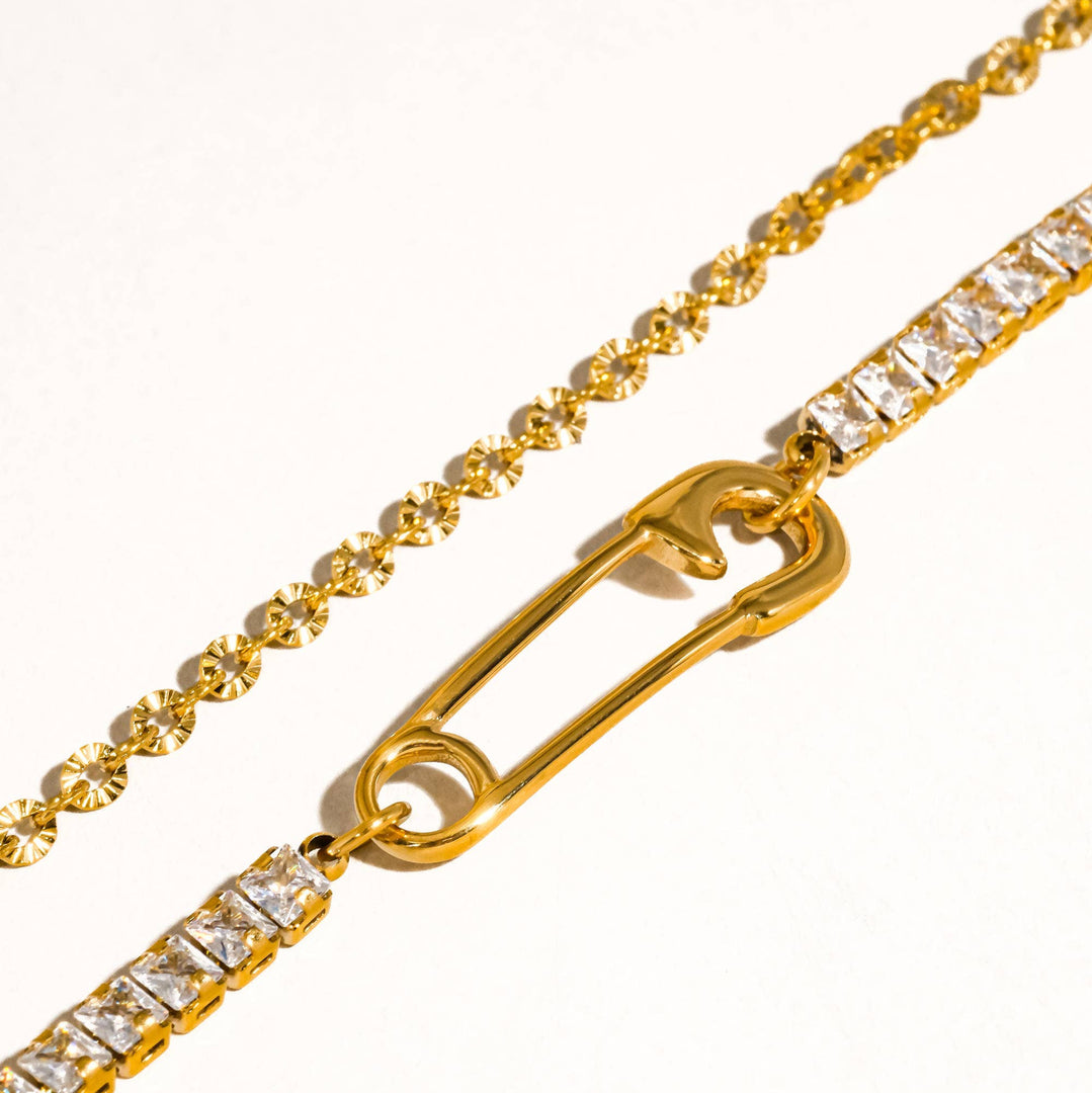 Gold chain with a safety pin design and clear stones on a white background