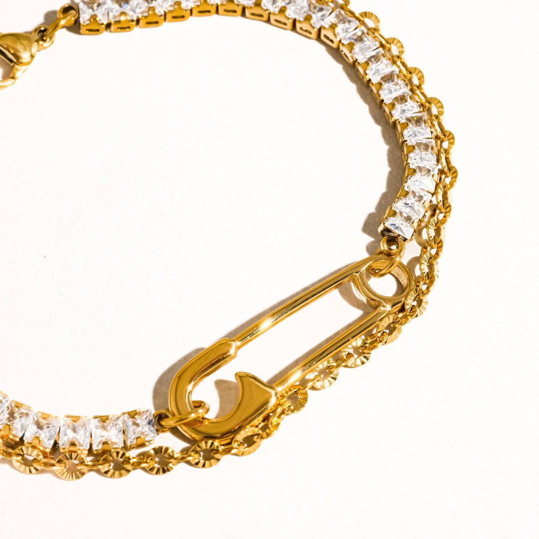 Gold bracelet with safety pin design and clear stones on a white background
