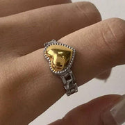 Gold heart-shaped ring on a finger against a neutral background