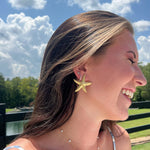 Load image into Gallery viewer, Woman wearing a starfish earring outdoors with a blue sky and greenery in the background
