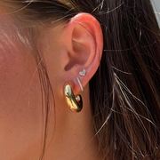 Close-up of an ear with gold earrings and a small heart-shaped earring.