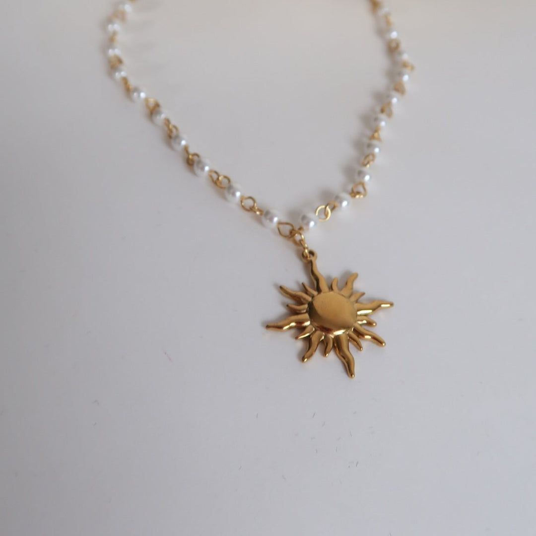 Gold sun-shaped pendant necklace on a light gray background
