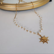 Gold necklace with a sun pendant on a white surface