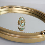 Load image into Gallery viewer, Gold-framed mirror with a ring on a gray background
