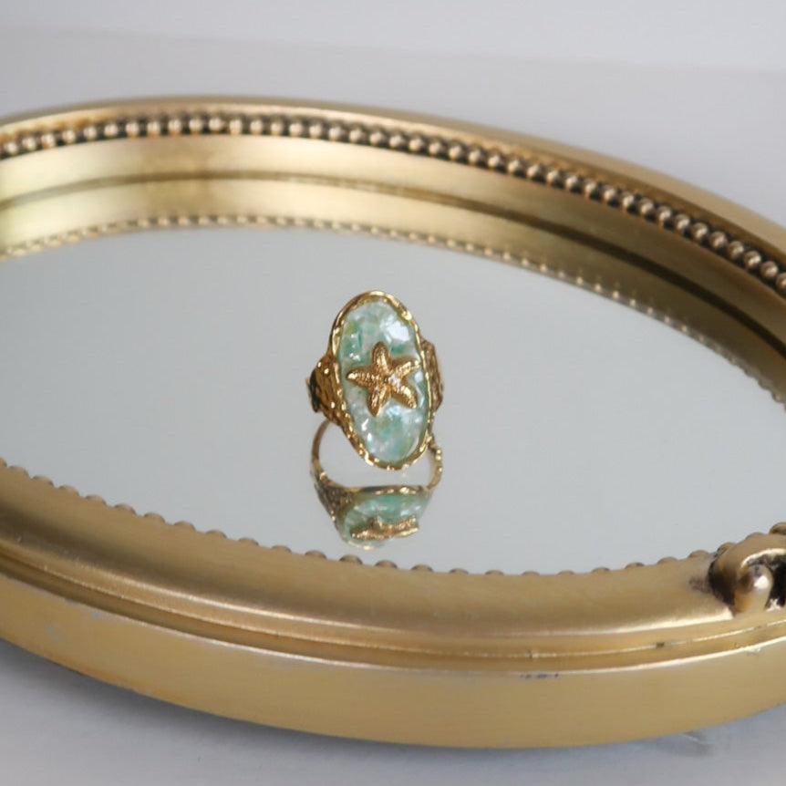 Gold-framed mirror with a ring on a gray background