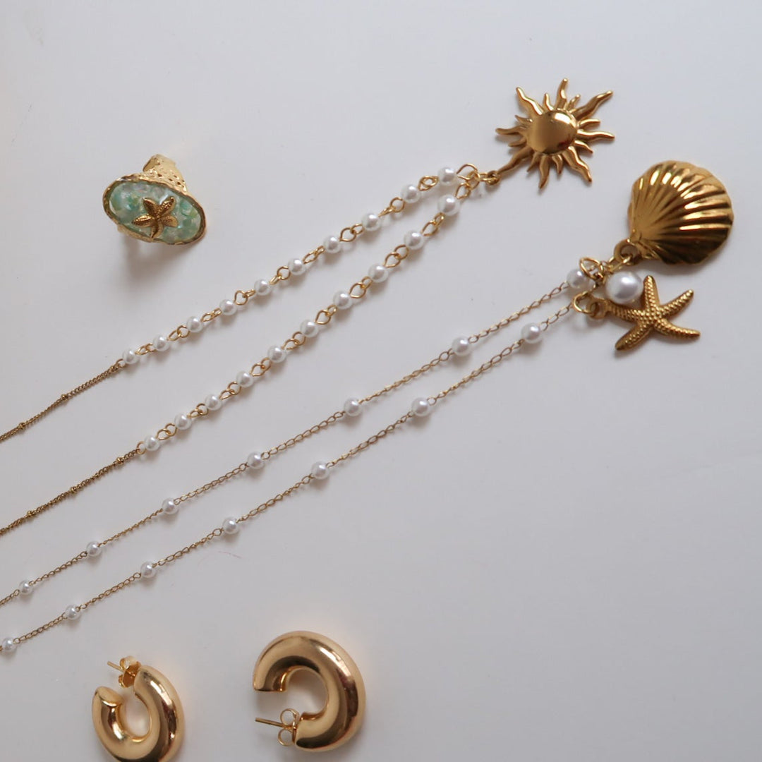 Gold jewelry set including necklace, earrings, and ring on a white surface with a gold mirror.