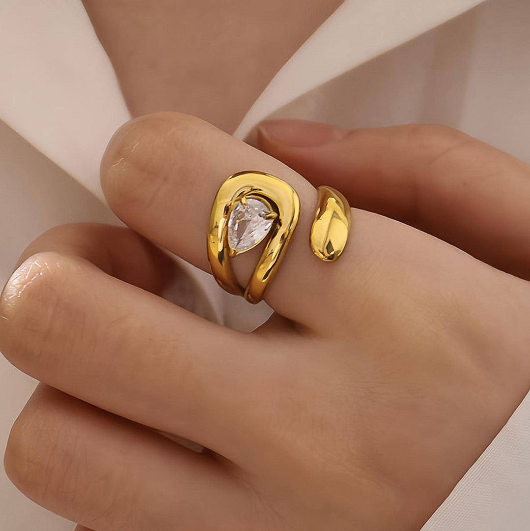 Gold ring with a clear gemstone on a hand against a neutral background